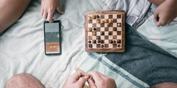 gracze wokół planszy z szachownicą i smartfonem na kocu